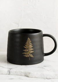 Black ceramic coffee mug featuring a gold fern leaf design in botanical print ceramic