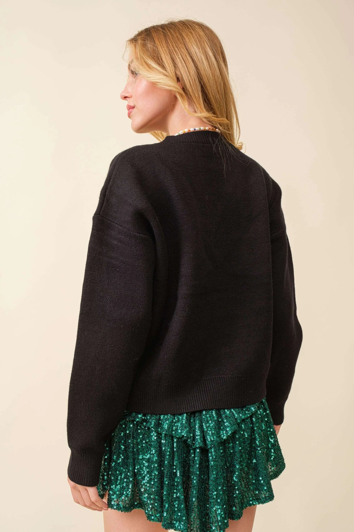 Black oversized sweater featuring a Christmas tree patch, styled over a sparkly green skirt