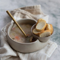 A bowl of chicken noodle soup with a gold spoon in a Stoneware Cracker & Soup Bowl