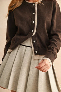 Brown cardigan with light-colored contrast button trim over a light gray pleated skirt