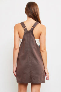 Brown leather overall dress layered over a white top, styled as a denim mini dress