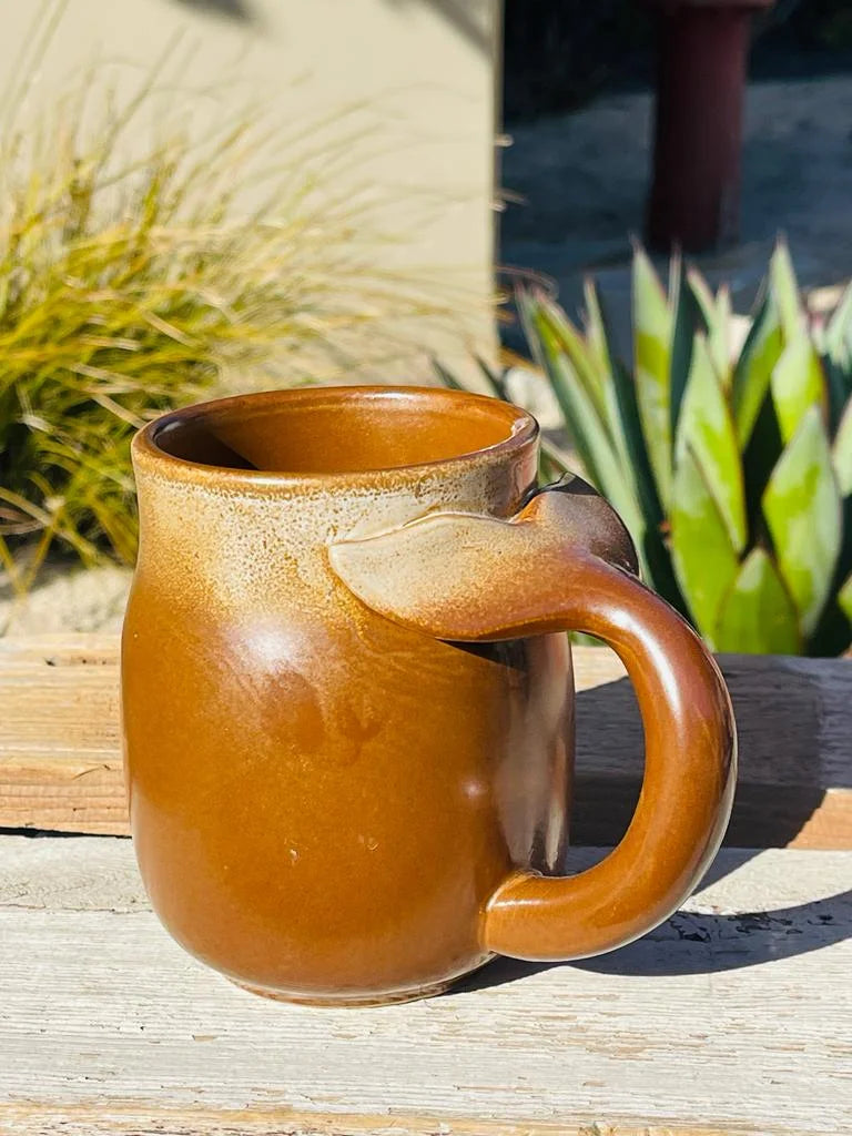 Brown stoneware mug with whale tail handle on a wooden table