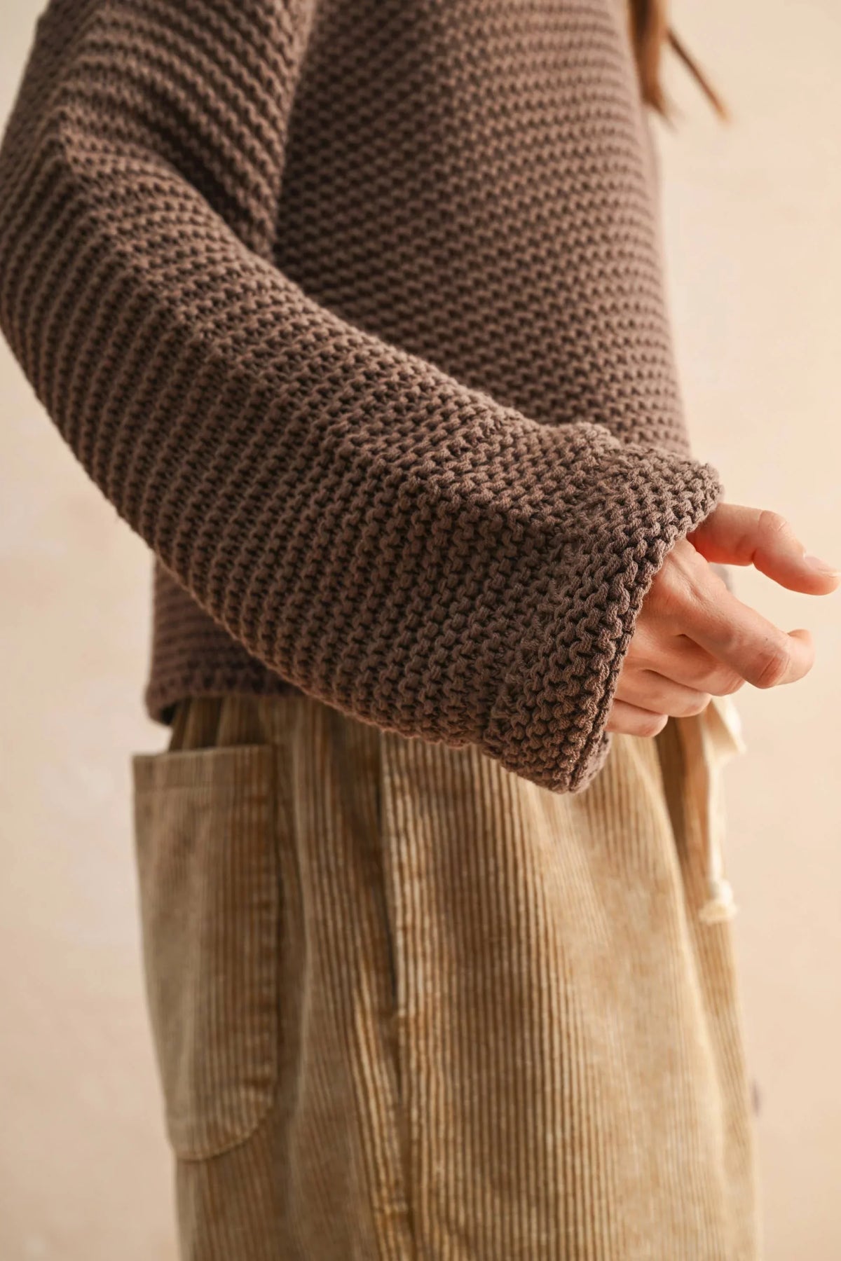 Brown round neck knitted sweater with ribbed cuffs, paired with corduroy pants