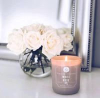 A serene White Rose Candle beside delicate flowers on a table from Daisy Lane