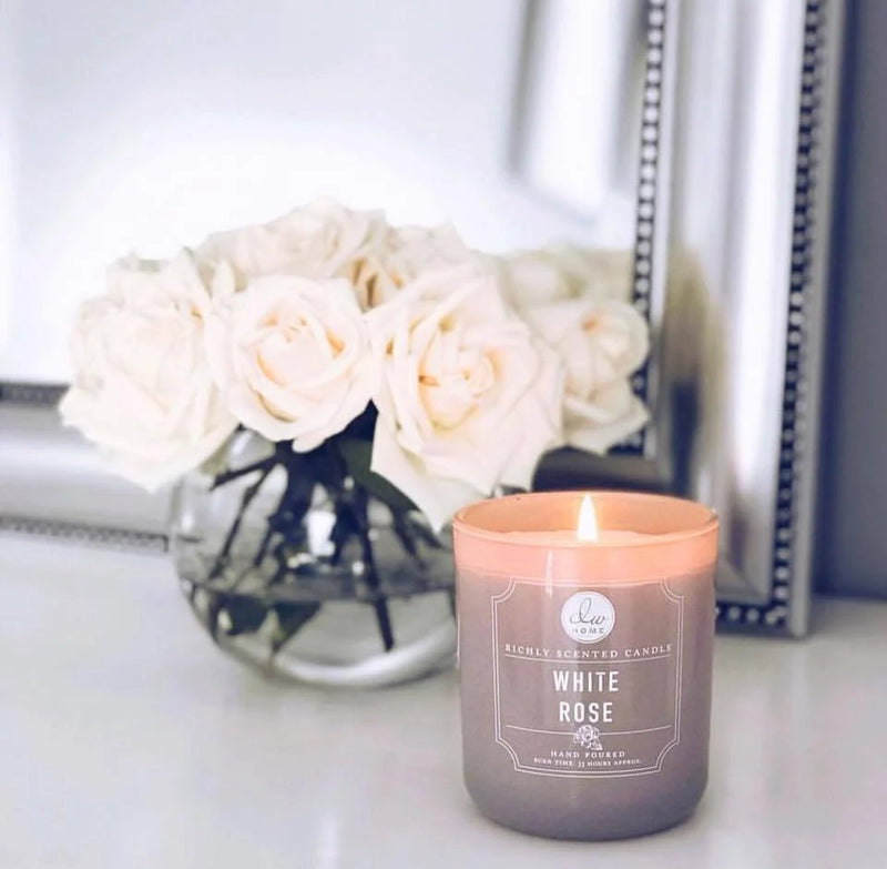 A serene White Rose Candle beside delicate flowers on a table from Daisy Lane