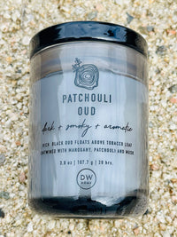 Candle on the ground with black label from Patchouli Oud Mini collection