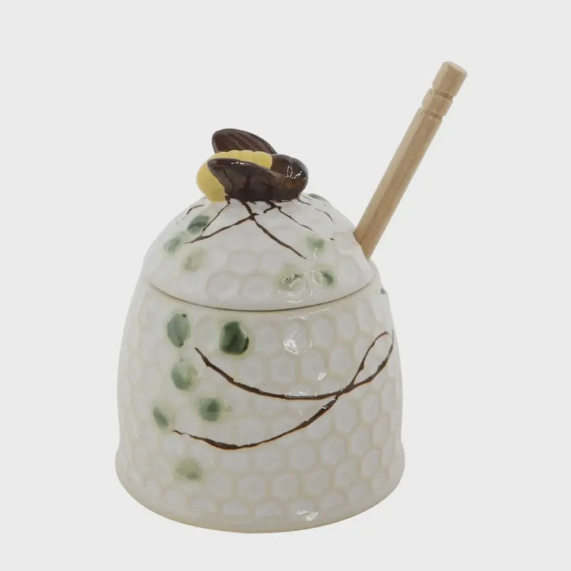 Hand painted honey jar with bee-shaped lid and wooden honey dipper for natural sweetness