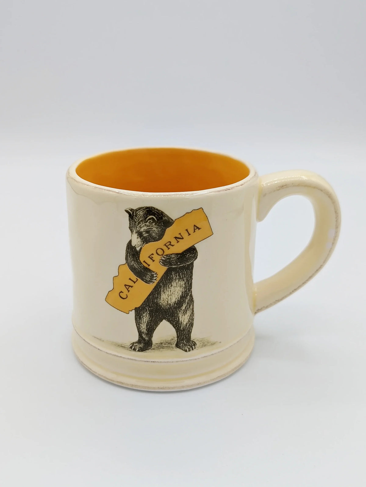 Ceramic mug featuring a California bear holding a sign in a bear hug design