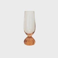 Ribbed footed champagne glass featuring a peach-colored ribbed glass base