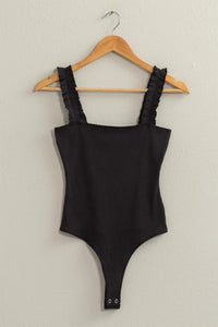 Close up of a black Ribbed Ruffle Strap Bodysuit hanging on a stylish hanger