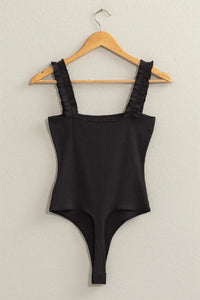 Close-up of a black Ribbed Ruffle Strap Bodysuit on a hanger showcasing its elegant design