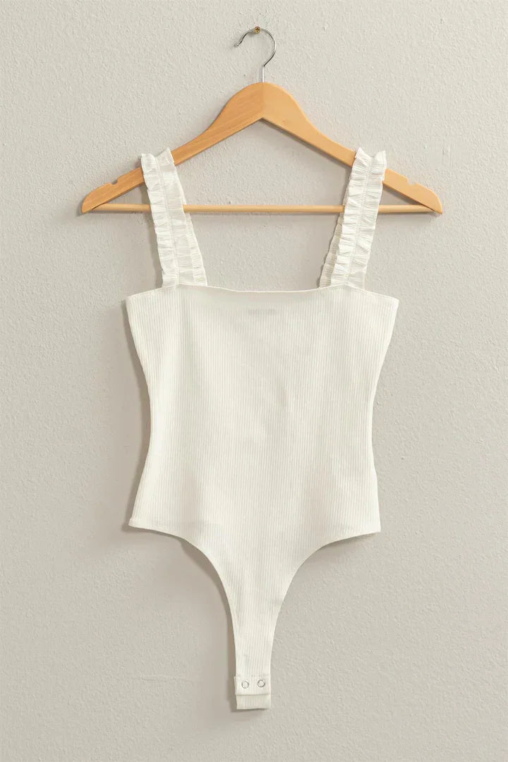 Close-up of a white Ribbed Ruffle Strap Bodysuit hanging on a hanger