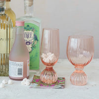 Collection of alcoholic beverage bottles and ribbed footed champagne glass in pink glassware