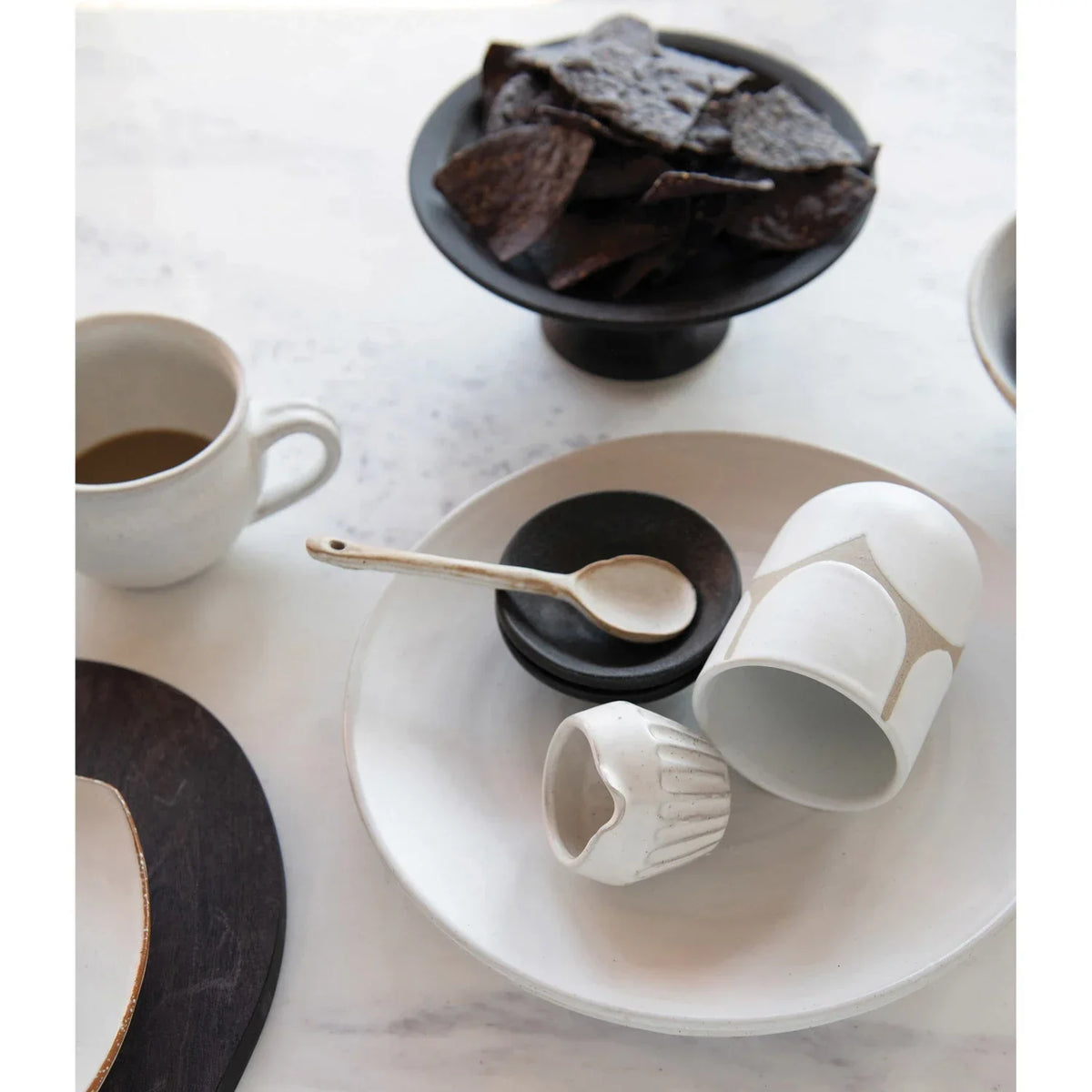 Ceramic collection featuring a stoneware mini bowl, cups, spoon, and dark chips