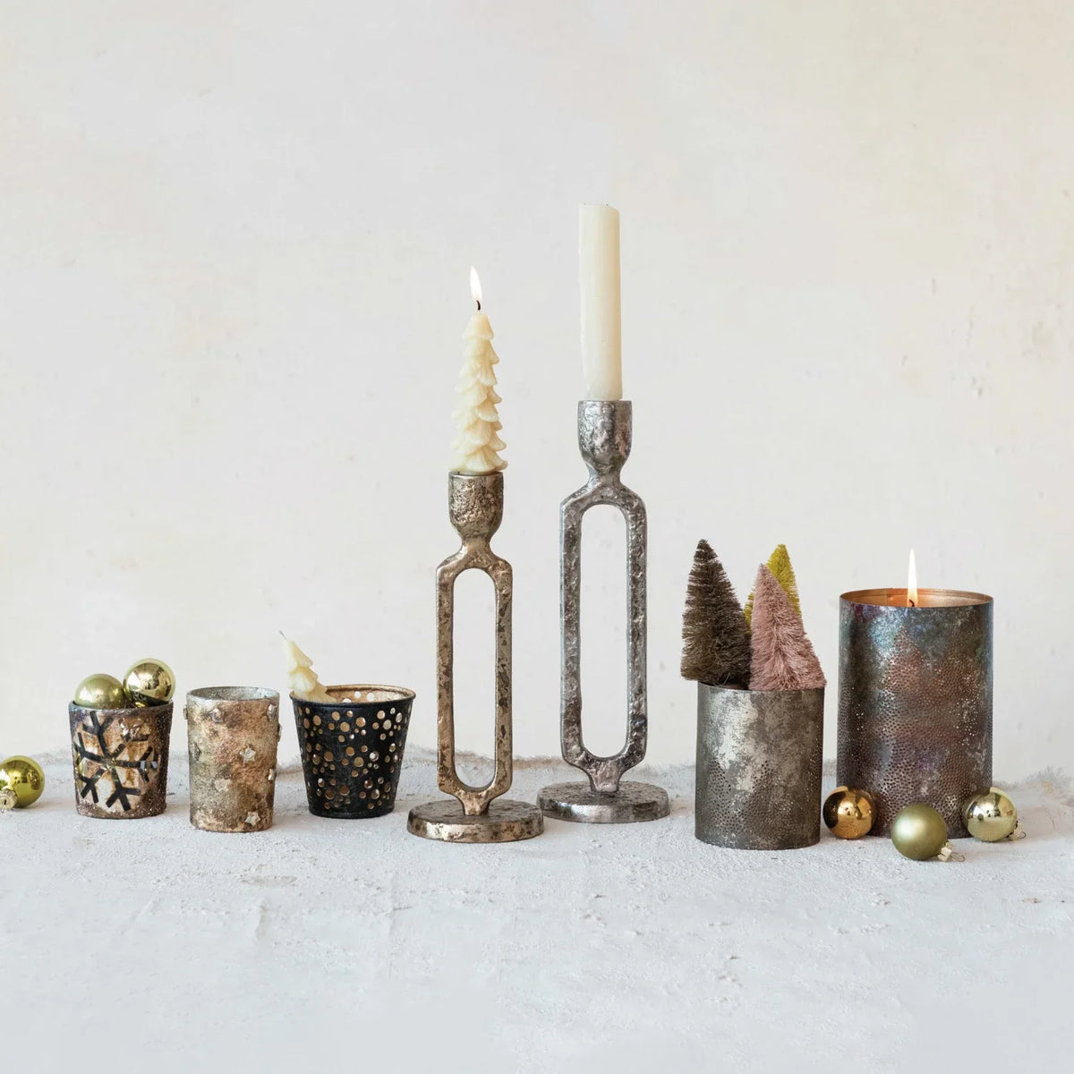 Collection of decorative candle holders, featuring a metal votive holder with tree cut-outs