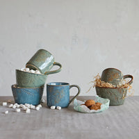 Collection of handmade ceramic mugs and cups in muted blue and green near embossed stoneware bowl