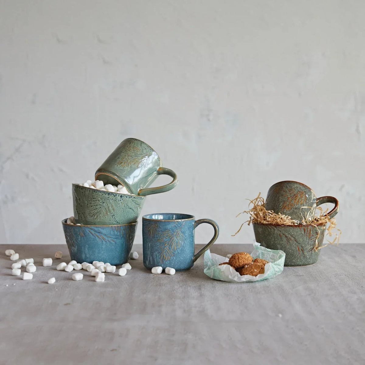 Collection of rustic embossed stoneware mugs and bowls in blue and green tones