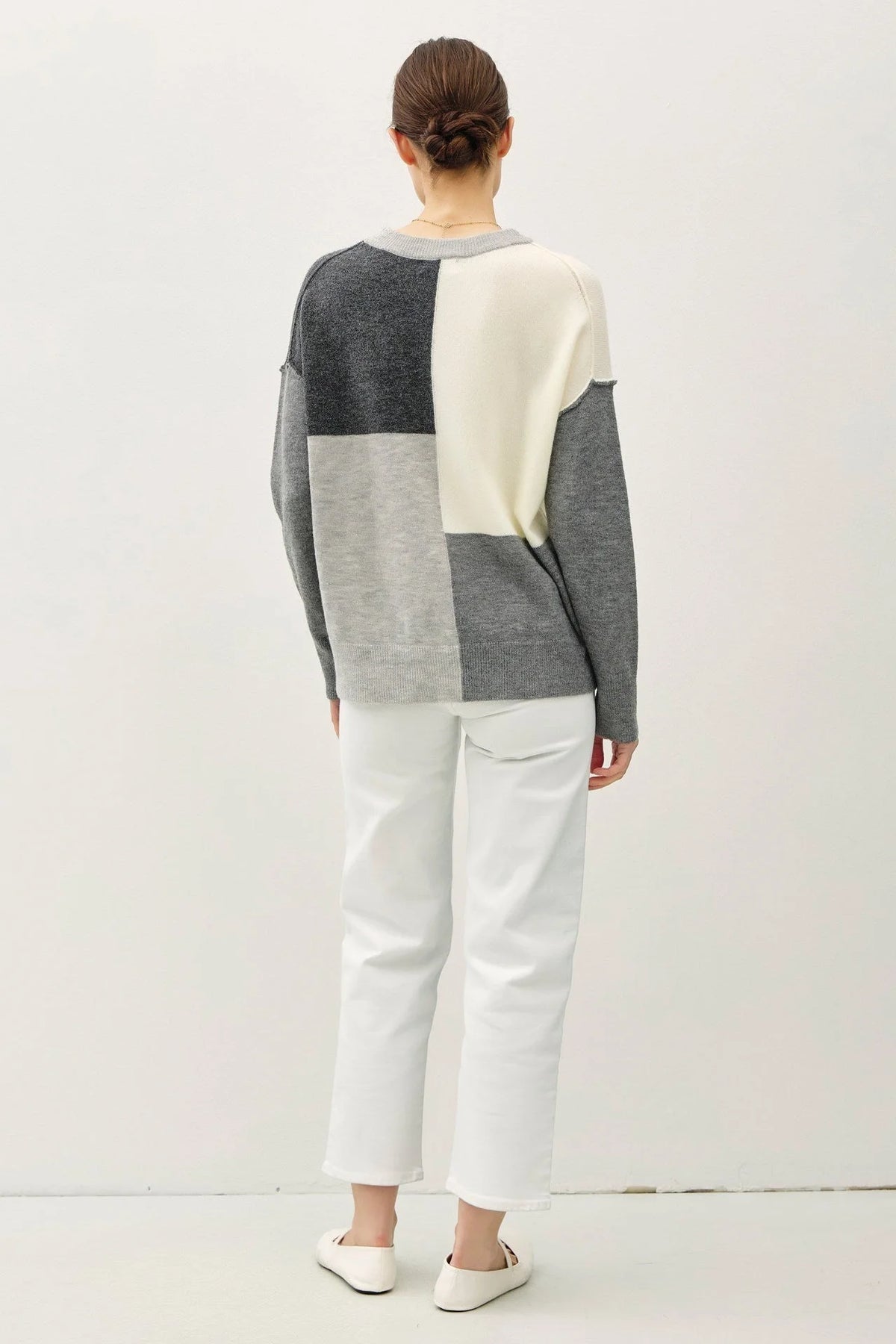 Color blocked crew neck sweater with geometric pattern over white pants