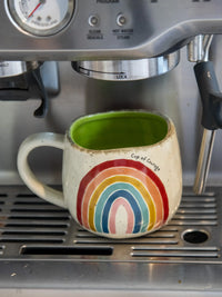 Colorful rainbow-patterned Artisan Rainbow Coffee Mug with bright green liquid for free spirits