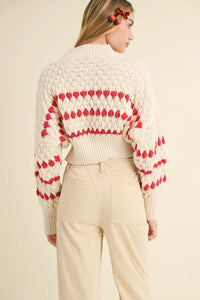 Cream-colored color popped sweater with red heart patterns on sleeves and back