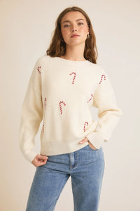 Cream-colored candy cane pullover sweater styled with blue jeans and a round neck long sleeve