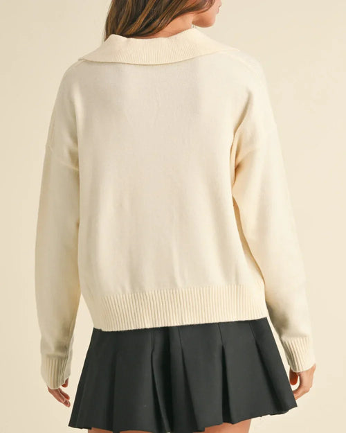 Cream-colored soft sweater paired with a pleated black skirt from Shop Daisy