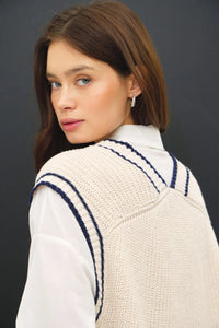 Cream-colored varsity style sweater vest with navy blue accent stripe and V-neck design