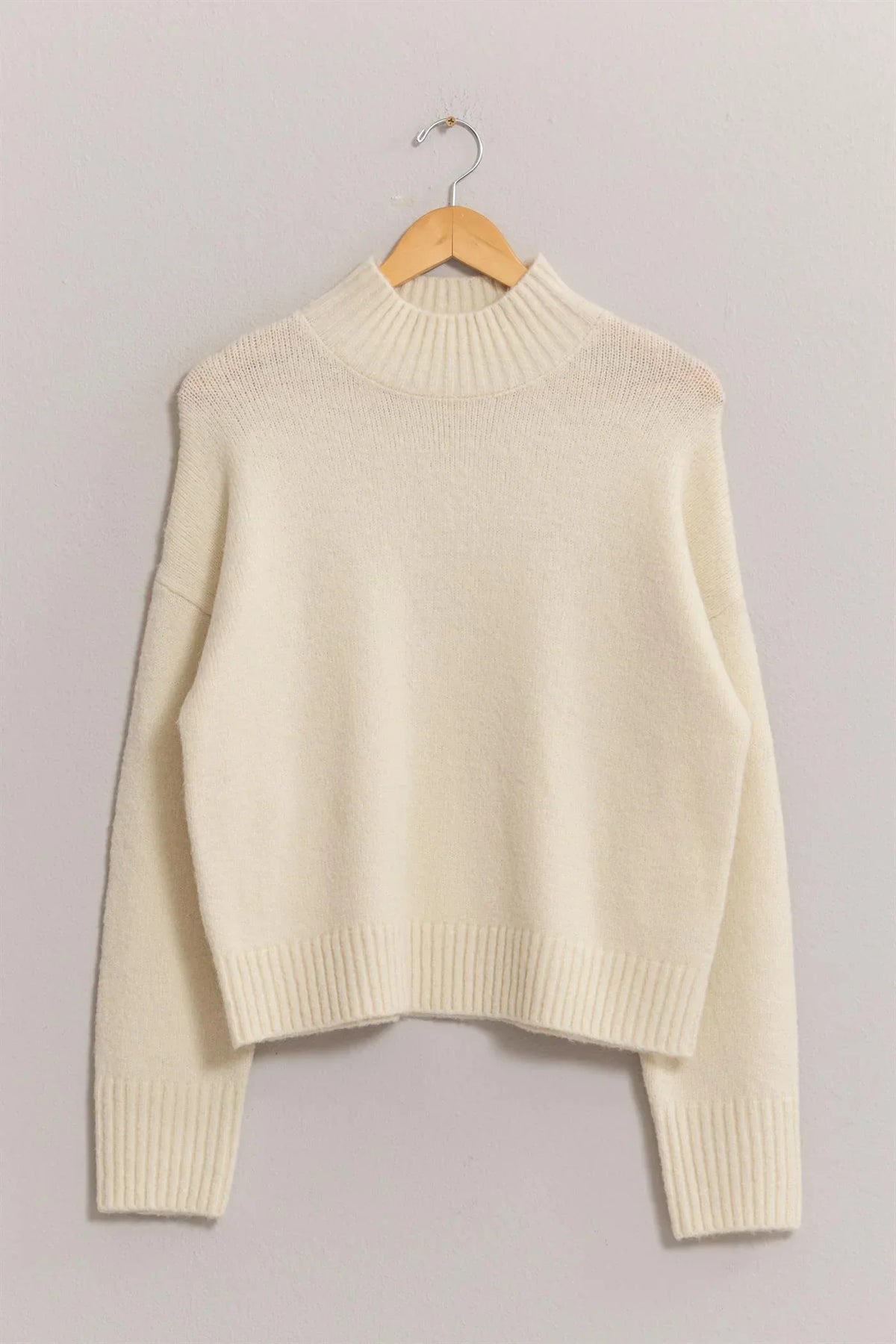 Cream-colored high neck sweater on wooden hanger from Shop Daisy women’s boho chic clothing