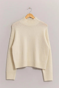 Cream-colored high neck sweater on wooden hanger from Shop Daisy women’s boho chic clothing