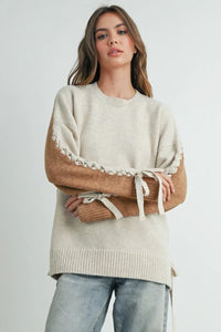 Cream-colored crew neck long sleeve pullover sweater with brown sleeves and lace-up details