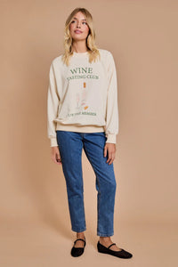 Cream-colored sweatshirt with WINE text paired with blue jeans and black flats in women’s boho chic clothing