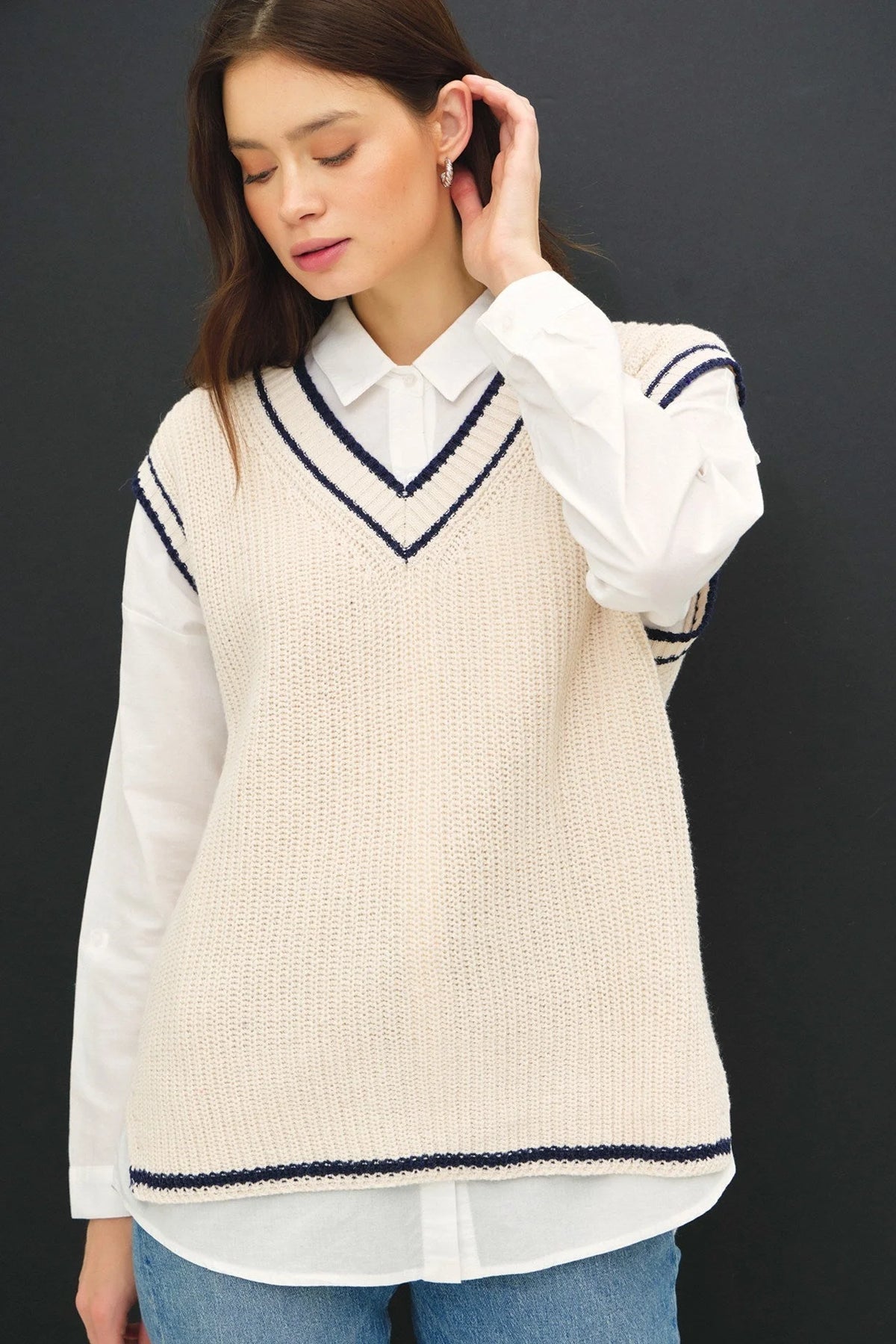 Cream-colored varsity style sweater vest with navy accent stripe over white shirt