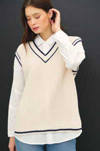 Cream-colored varsity style sweater vest with navy accent stripe over white shirt