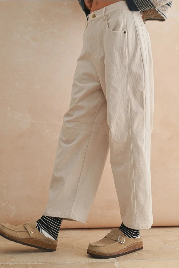 Cream-colored corduroy barrel pants with striped socks and brown loafers