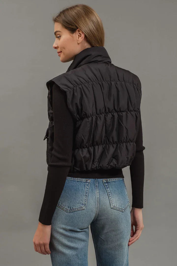 Cropped puffer vest featuring snap button closure, styled with jeans and a long-sleeved top