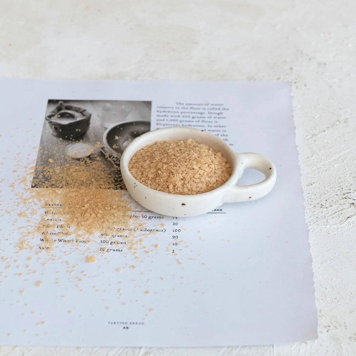 A stoneware dish with handle holding a cup of coffee beside a book on a table