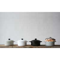 Four colorful stoneware mini bakers with lids arranged on a wooden surface