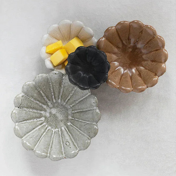 Four colorful stoneware flower bowls in white, yellow, black, and brown designs