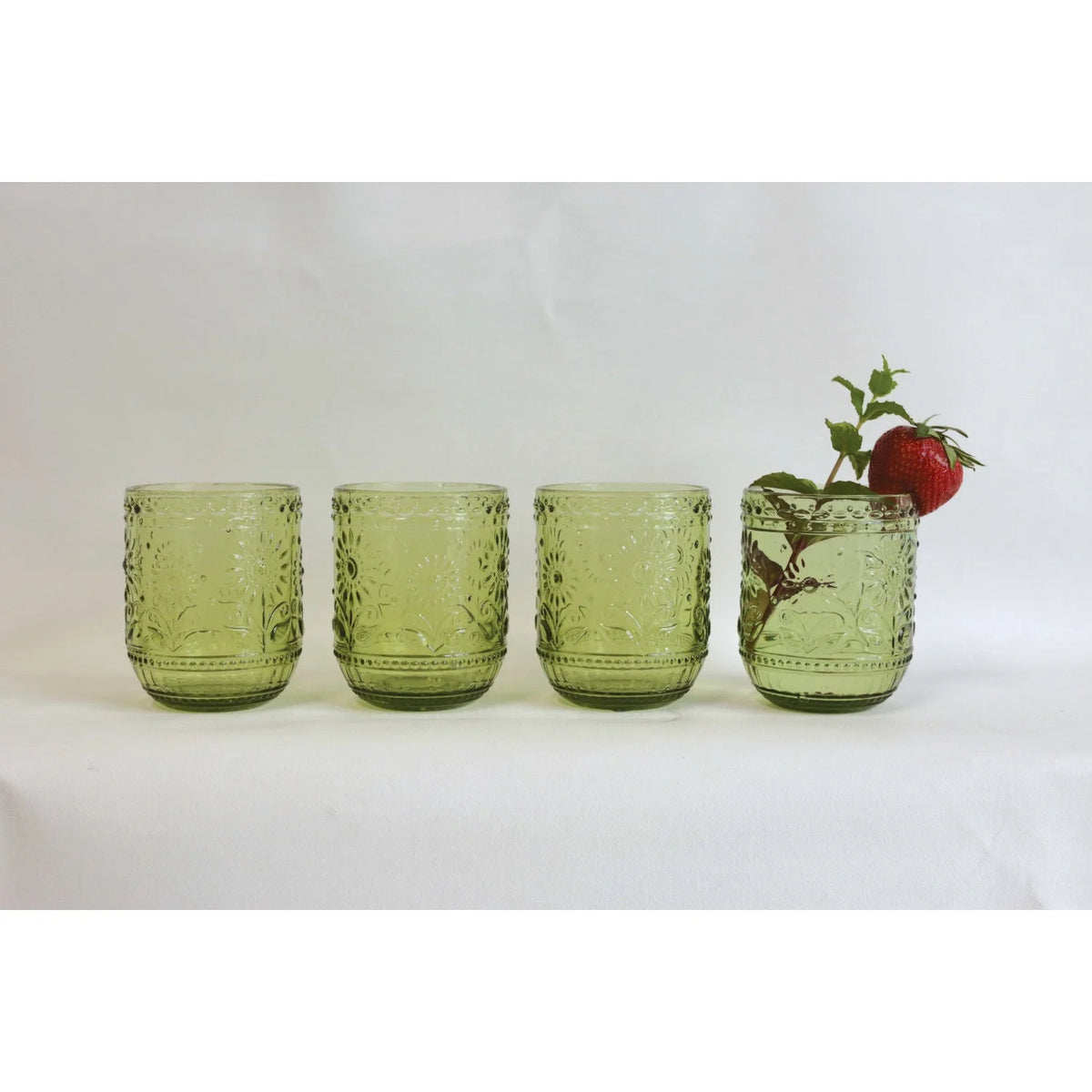 Four green embossed drinking glasses with a strawberry and mint in the last glass