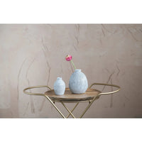 Gold-framed circular side table featuring a terracotta vase with engraved lines and a pink flower