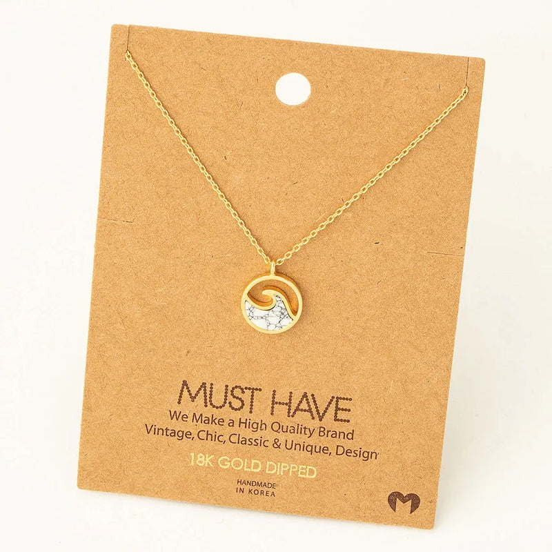 Gold pendant necklace featuring a wave coin design with crystal accents on display card