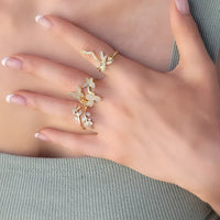 Gold-toned rings with butterfly and leaf designs on a hand, featuring the TIED BOW RIBBON GOLD RING