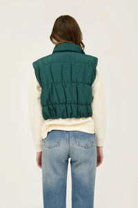 Green quilted puffer vest with snap button, styled over white top and blue jeans