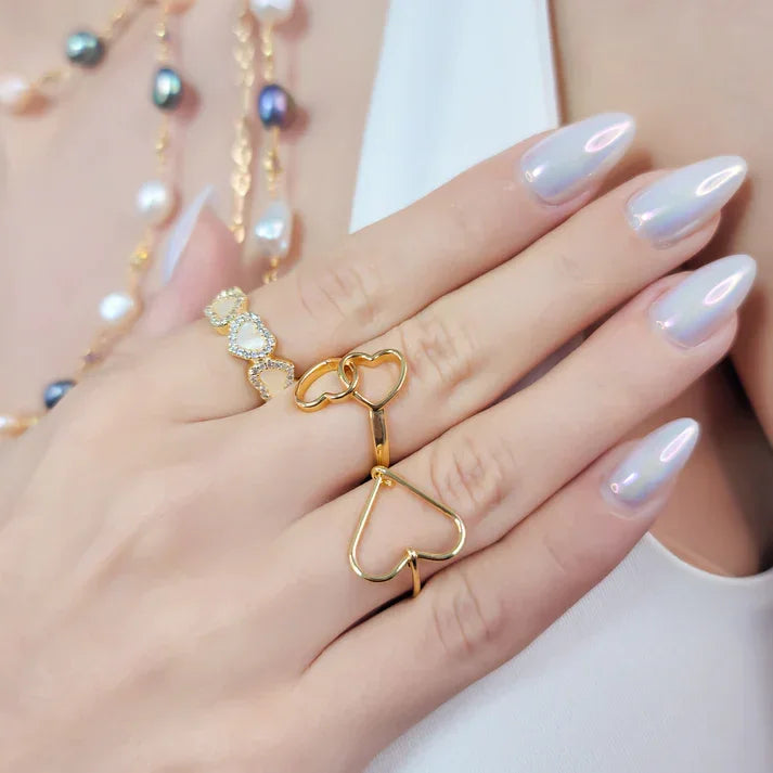 Hand wearing heart ring adjustable with gold heart-shaped rings, pearl necklace, polished nails
