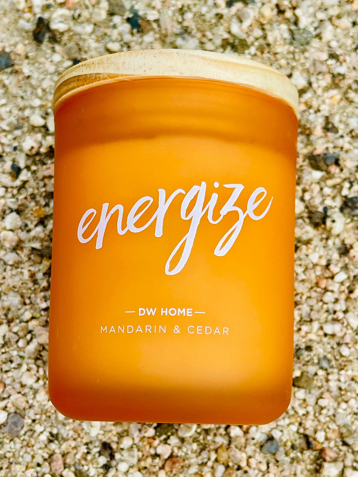 A jar of orange liquid by the beach for Energize Mandarin & Cedar Mini Candle