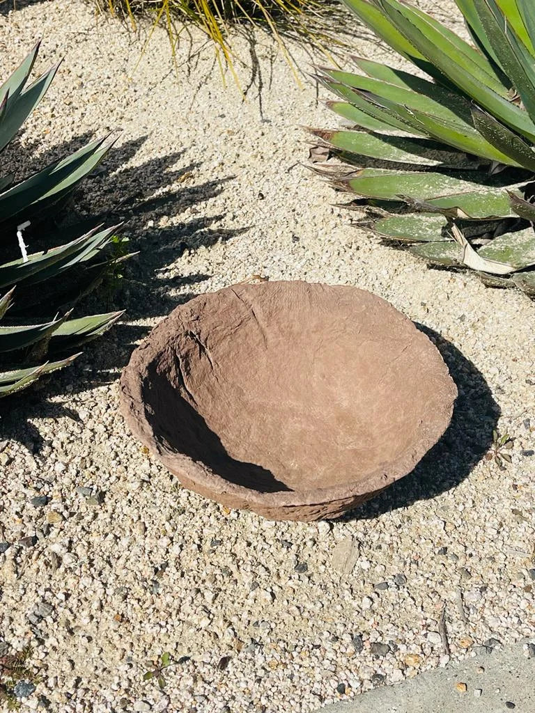 A large rock in a garden beside a decorative handmade paper mache bowl