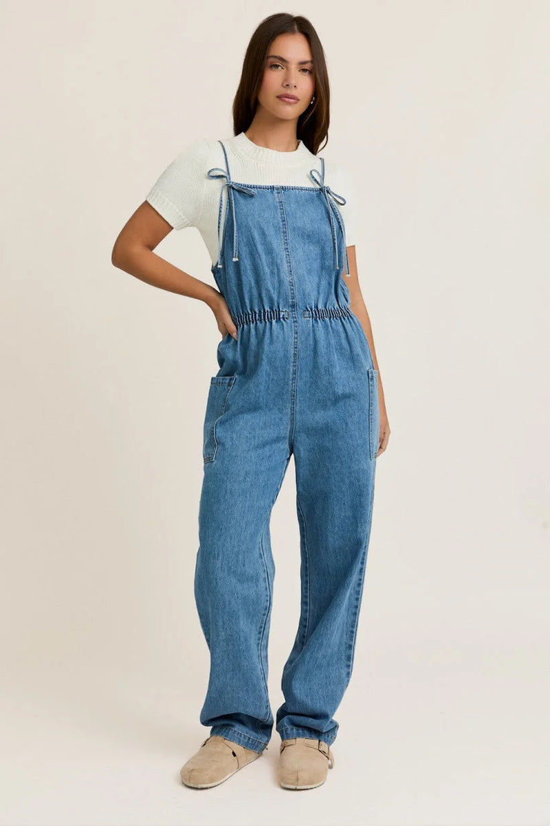 Light blue denim overalls with bow ties, styled with a white t-shirt and beige shoes