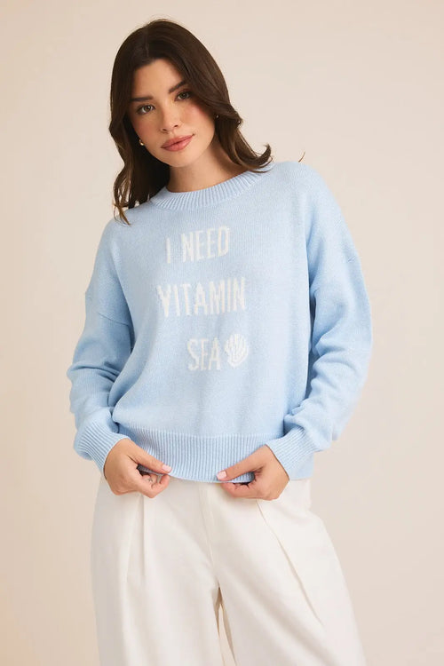 Light blue Vitamin Sea sweater with white text paired with white pants