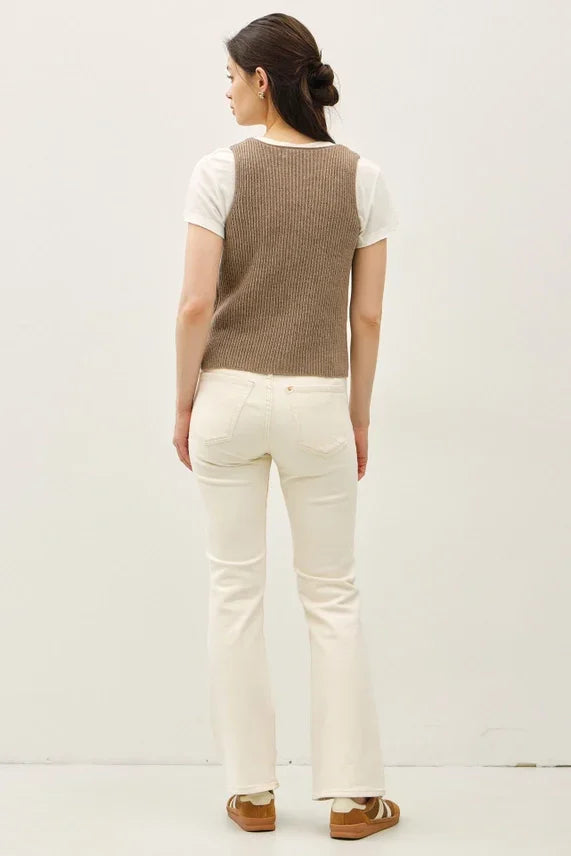 Light brown chunky V neck sweater vest with neck button over white top and off-white jeans