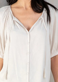 Light-colored floral puff sleeve top with V-neck, button front, and tasseled drawstrings